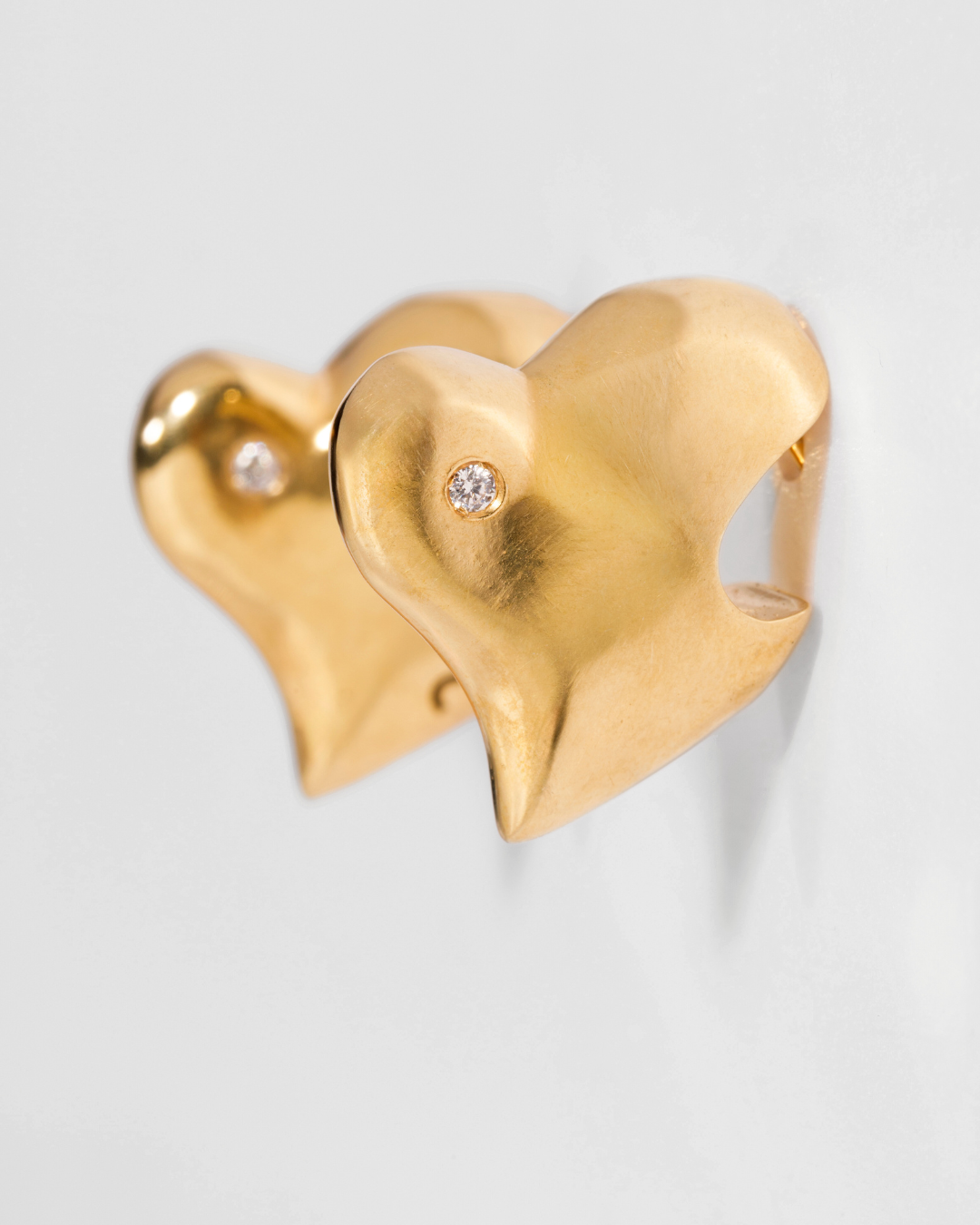 Gold heart-shaped earrings with a diamond on a light gray background